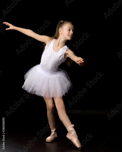 Cute little girl in a tutu and pointe shoes is dancing in the studio on a black background.