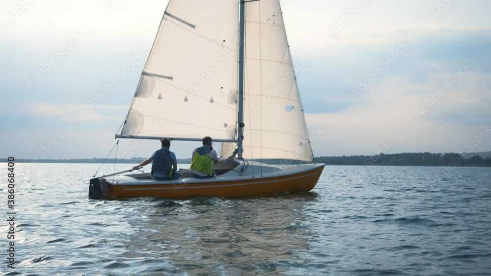 Sailboat. Beautiful yacht with two sailors friends moving across wide lake in cinematic landscape. Marine scenery, calm sea, freedom and inspiration.