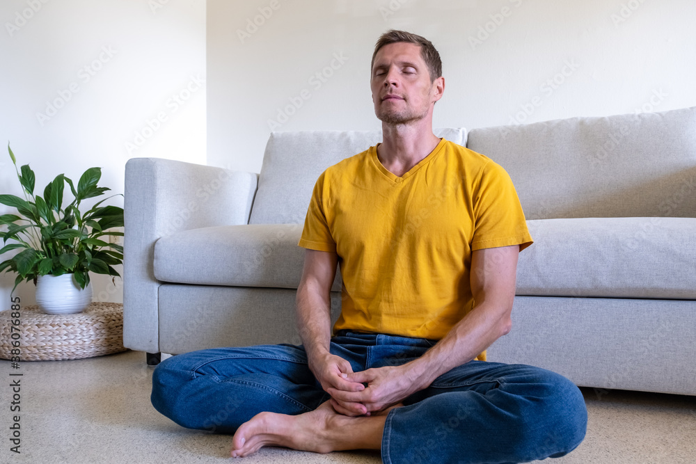 Handsome man with eyes closed sitting on floor in Lotus Pose and meditating at home Handsome man with eyes closed sitting on floor in Lotus Pose and meditating at home