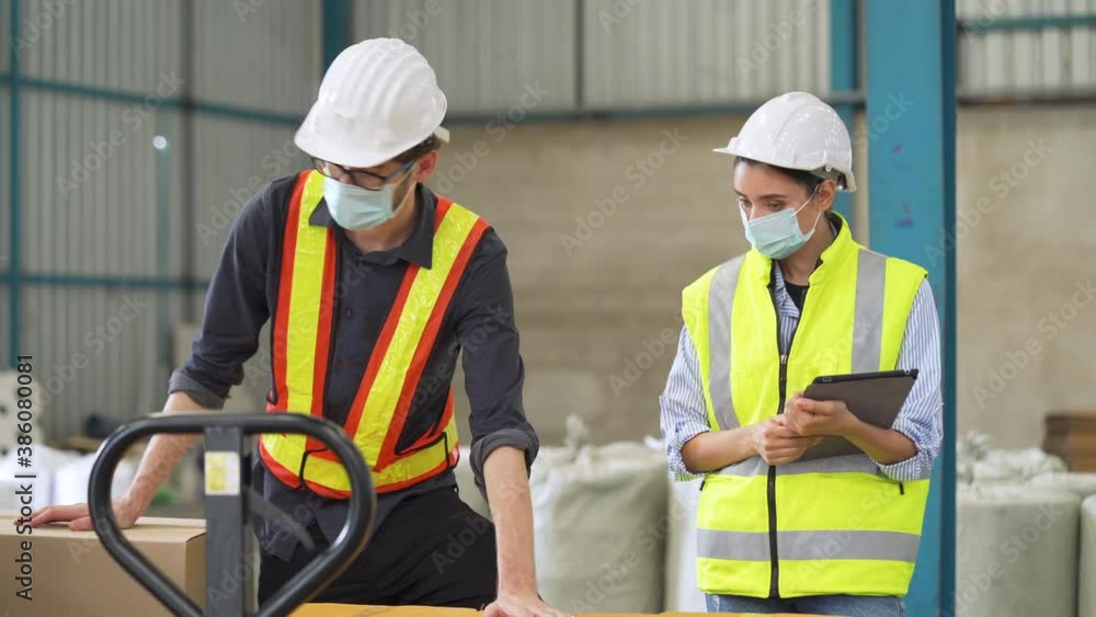 Female Inventory Manager checking stock on Digital Tablet. Man warehouse worker with hard hat safety helmet at storage buildings