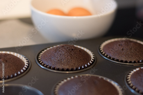 Close up of chocolate cupcakes in baking trays with a bowl of eggs in the background