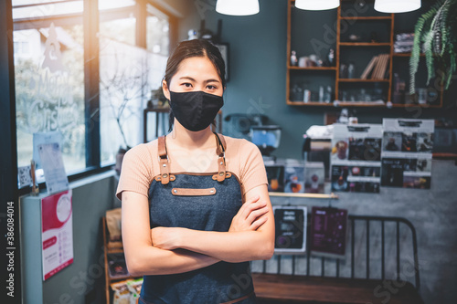 New normal Asian barista woman worker small business owner café restaurant store shop wearing facemask protection COVID-19 coronavirus pandemic cheerful arms crossed smiling happy copy space portrait