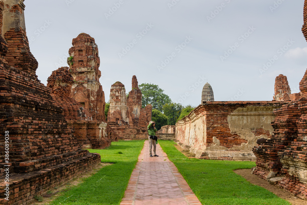 A tourist man taking picture of the old ruin at Wat Phra Mahathat, Ayutthaya Historical Park, Thailand Raining Season