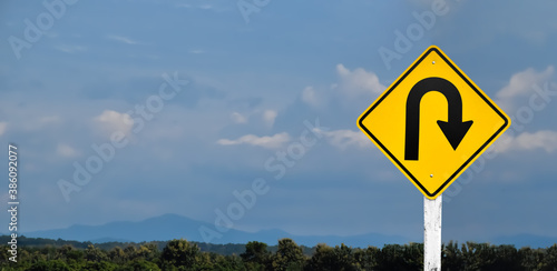 U-turn sign on white pole with clouds and blue sky background.