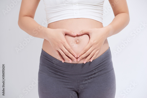 happy pregnant woman holding hands in heart shape on belly