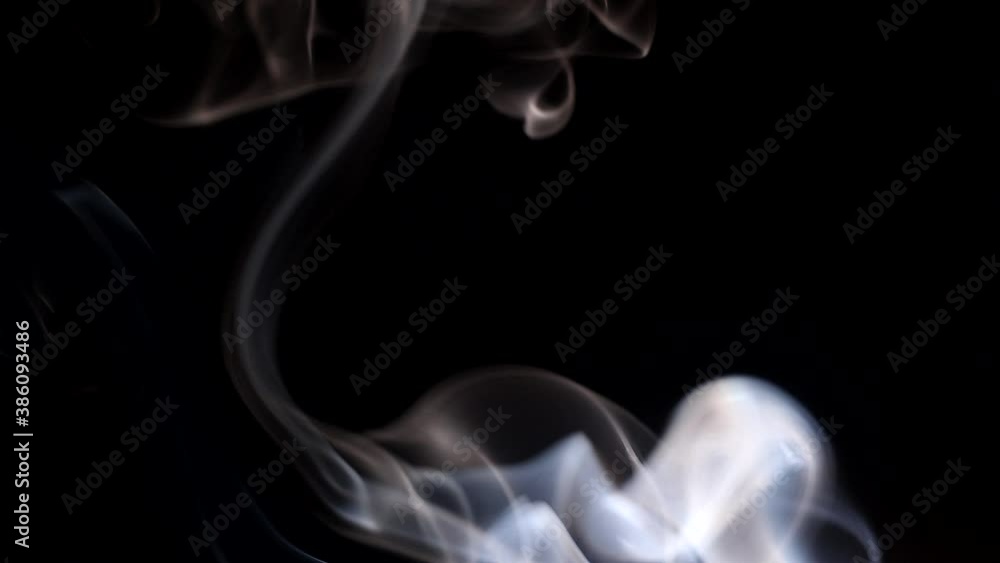 Smoke streaming in the dark from a burning incense stick. Whimsical curls of smoke on a dark background. A soothing atmosphere of relaxation. Smoke streaming in the dark from a burning incense stick. Whimsical curls of smoke on a dark background. A soothing atmosphere of relaxation.