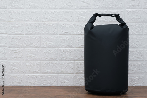 Close up black plastic waterproof dry bag on desk over white brick wall free from copy space.