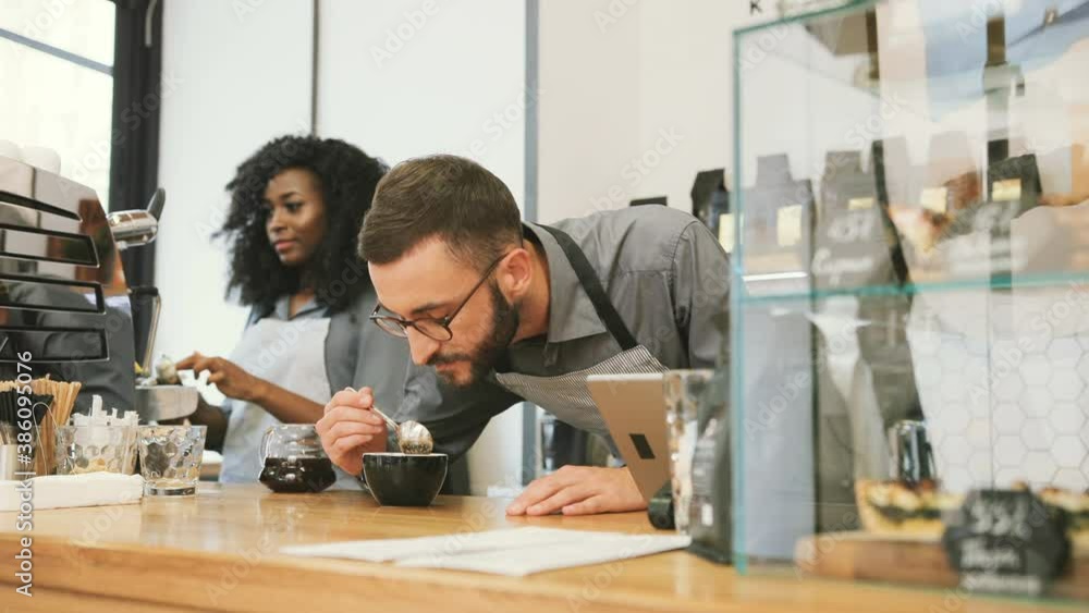 Young Caucasian barista is capping coffee in coffee shop. Beautiful barista girl wipes holder from coffee machine. Young Caucasian barista is capping coffee in coffee shop. Beautiful barista girl wipes holder from coffee machine.