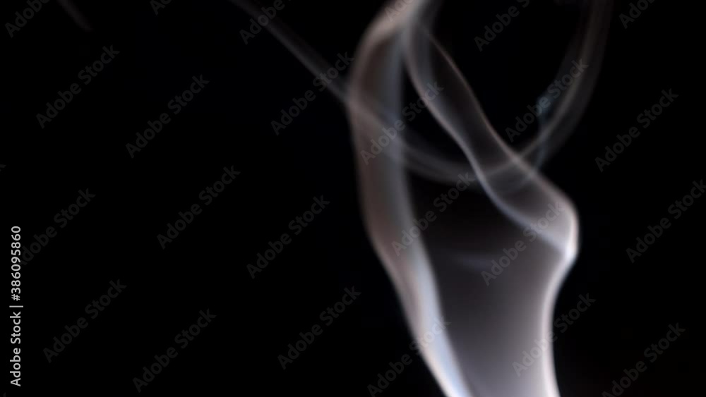 Smoke streaming in the dark from a burning incense stick. Whimsical curls of smoke on a dark background. A soothing atmosphere of relaxation. Smoke streaming in the dark from a burning incense stick. Whimsical curls of smoke on a dark background. A soothing atmosphere of relaxation.