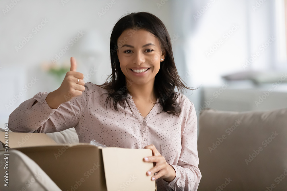 Portrait of smiling African American woman show thumb up unpack unbox post package shopping online from home. Happy biracial female consumer recommend good delivery service or shipping company. Portrait of smiling African American woman show thumb up unpack unbox post package shopping online from home. Happy biracial female consumer recommend good delivery service or shipping company.