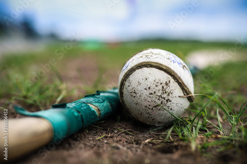 A hurley and a sliothar lie in the grass with a out of focus background photo