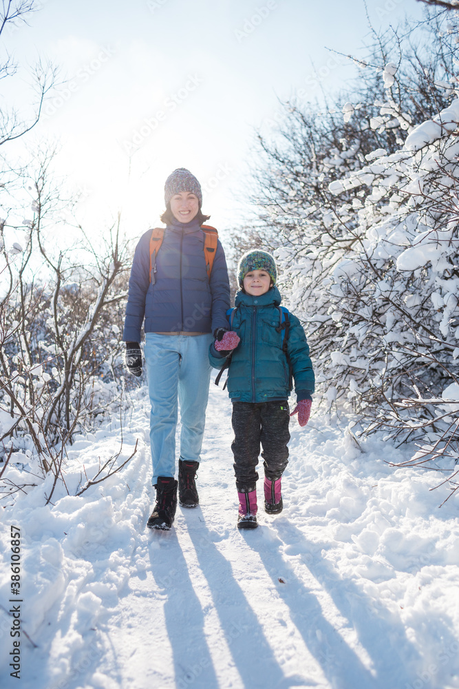 A child with a backpack walks with mother in a snowy forest A child with a backpack walks with mother in a snowy forest