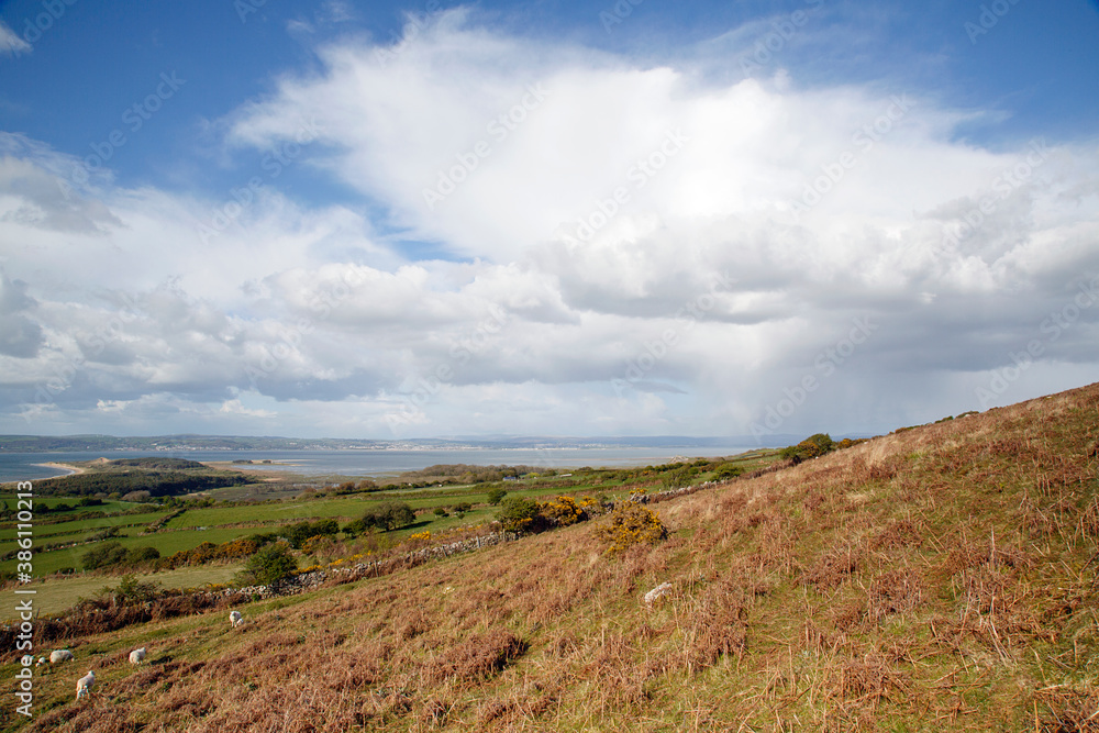 Beautiful Welsh countryside overlooking the north Gower coastline with blue skies, white clouds and sporadic rain.