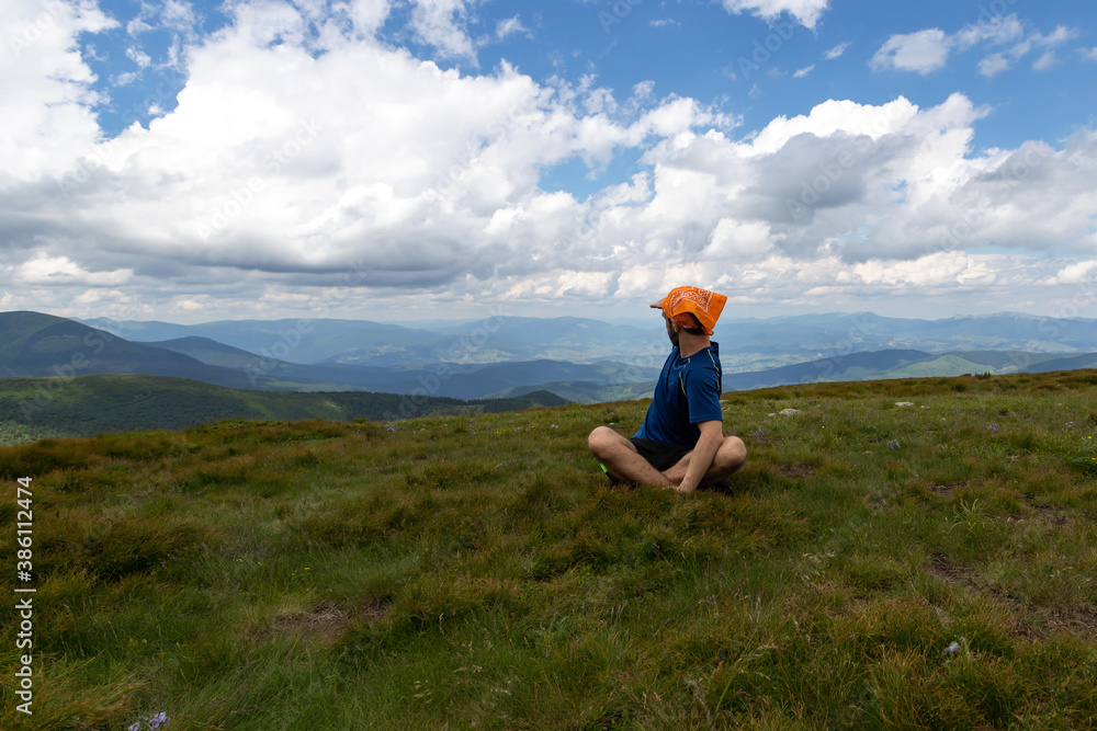 Guy looks at the beautiful mountains, sitting in the meadow.