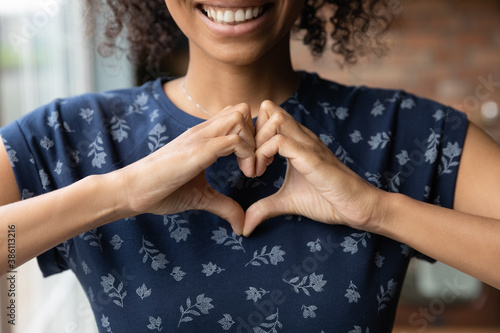 Crop close up of happy African American woman feel grateful thankful show heart sign spread love and care. Smiling biracial female volunteer make hand gesture support ill sick people patients. photo
