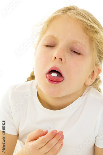 A little girl in a clean white T-shirt swallows a pill, the pill lies on her tongue. Covid-19 concept, virus, disease, treatment.