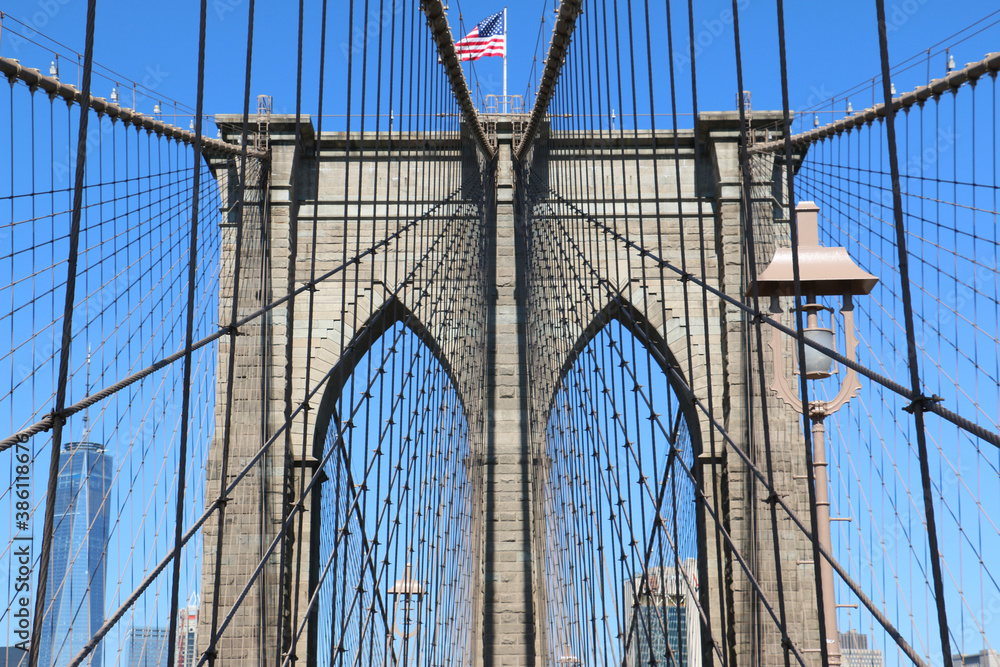 Fototapeta premium Brooklyn Bridge in New York City close up, One World Trade Center visible. American US Flag and blue sky