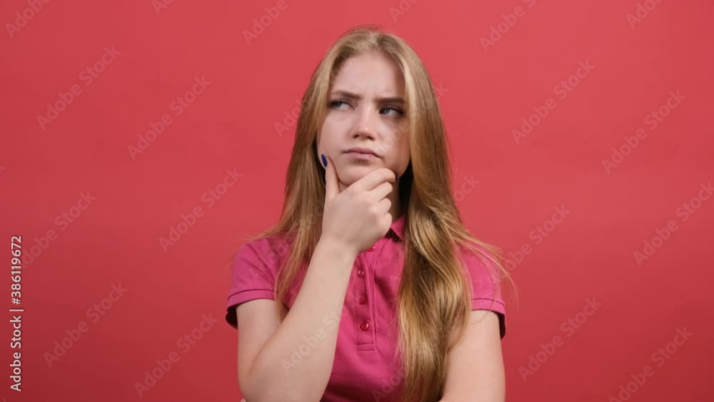 Close up of a serious young woman sits with her hand next to face and looks aside as she thinks about important things, isolated over red background. Close up of a serious young woman sits with her hand next to face and looks aside as she thinks about important things, isolated over red background.
