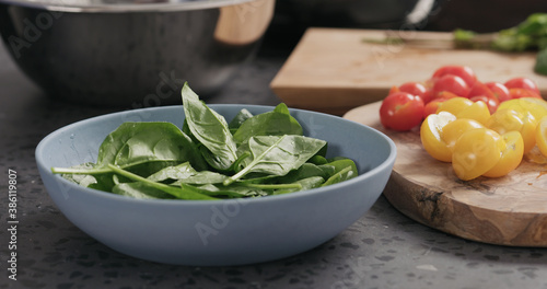 Closeup making salad with spinach, tomatoes and mozzarella in ablue bowl on concrete countertop