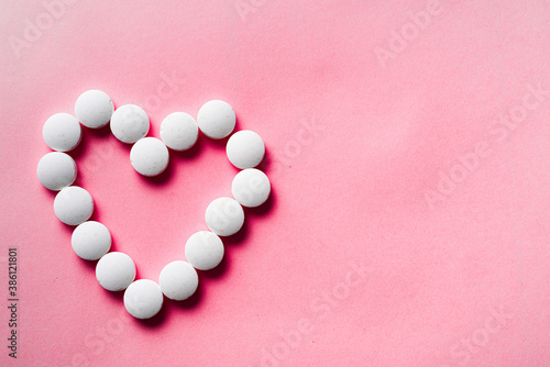 many white pills from heart on a pink background. accept gifts concept. Cardiology or love concept