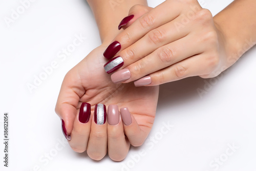 Gel manicure. Beige and burgundy manicure with a wide silver strip on long square nails close-up on a white background. 