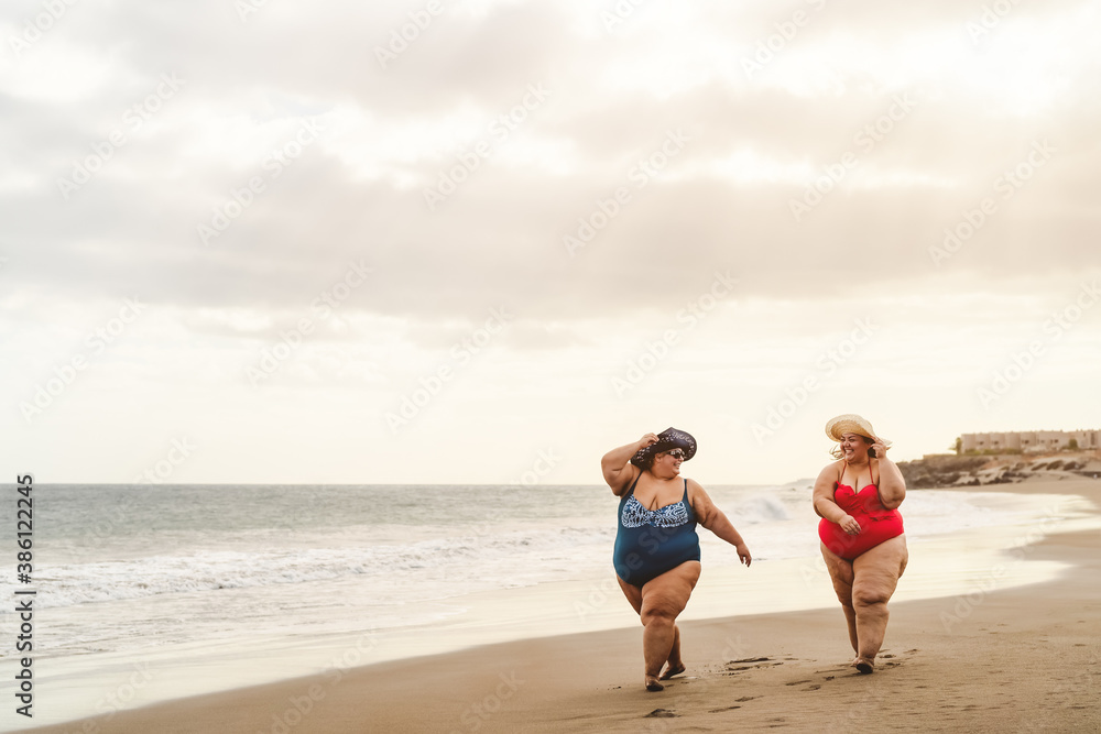 Happy plus size women having fun walking on the beach - Curvy confident people lifestyle concept