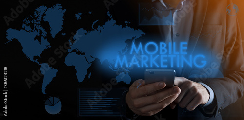 Businessman holding a smartphone with inscription MOBILE MARKETING with different graphs and warld map on the background.m-banking and omni channel,online shopping. photo