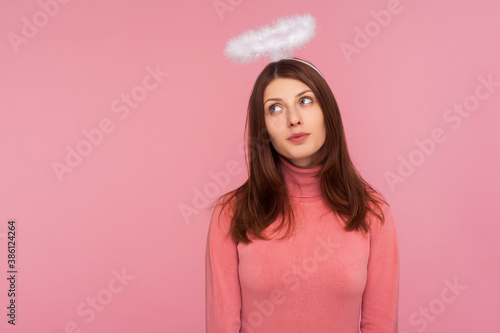 Adorable cute brunette woman in pink sweater standing with halo over head, angelic innocent expression, faith. Indoor studio shot isolated on pink background