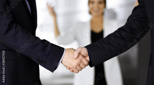 Unknown businesspeople are shaking their hands after signing a contract, while standing together in a modern office, close-up. Business communication, handshake, and marketing concept © cameravit
