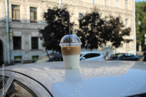 Glass of ice coffee latte on the roof of a white car on a sunny day