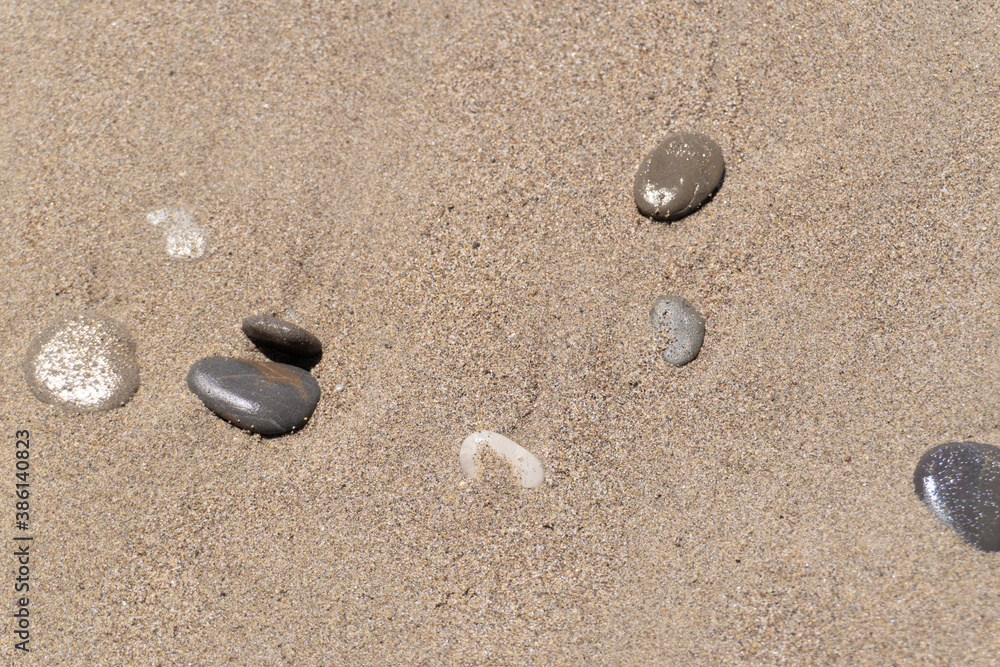 Small rocks scattered on beach sand close up. Shallow depth of field. Top view. Wet stones on bright beach sand Small rocks scattered on beach sand close up. Shallow depth of field. Top view. Wet stones on bright beach sand