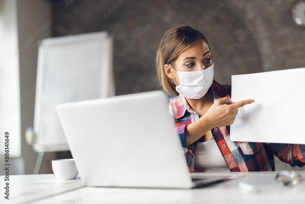 Young businesswoman wears mask while having a video conference call with someone over the computer in the office Young businesswoman wears mask while having a video conference call with someone over the computer in the office