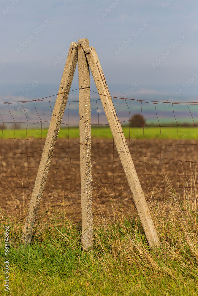 Concrete thin posts in the field between which there is a tensioned fence. The landscape is in the background. Concrete thin posts in the field between which there is a tensioned fence. The landscape is in the background.