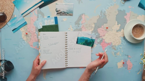 Horizontal from above zoom-in flat lay footage of woman putting tick in checklist doing travelling preparations before flight photo