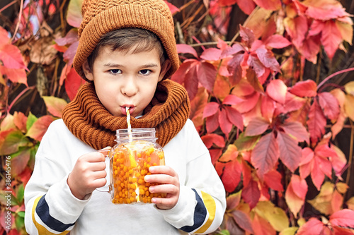 cute fashionable boy holding a sea buckthorn drink on a background of wild grapes.