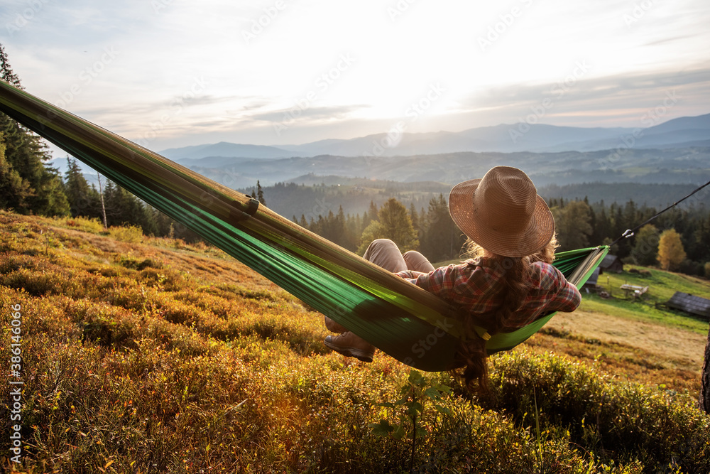 Woman hiker resting after climbing in a hammock at sunset - obrazy, fototapety, plakaty 