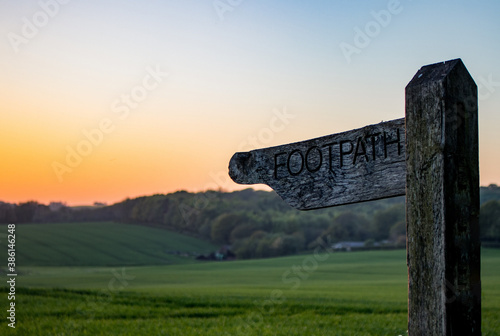 Canvas Print A wooden footpath sign in the english countryside at sunset with rolling green h