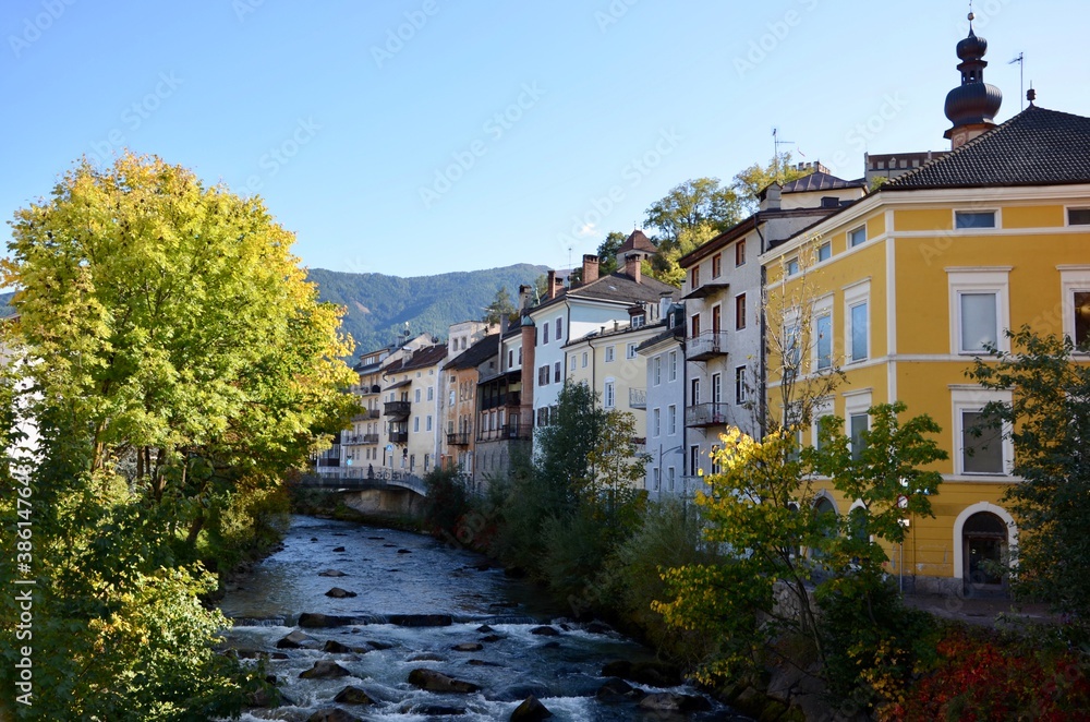 Historic buildings in the old town of Bruneck (Brunico) in the valley Pustertal in South Tirol, river Ahr in the middle, autumn landscape, a sunny day, blue sky background