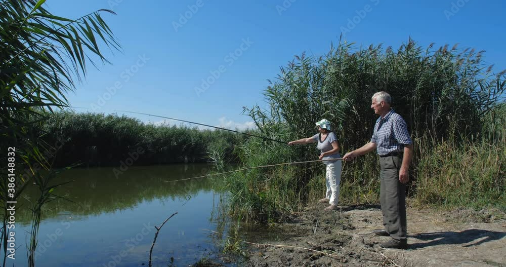 Active happy and healthy elderly European couple in casual clothes fishing with a rods near the lake on a warm summer day with their two granddaughters. slow motion 4k 50 fps Active happy and healthy elderly European couple in casual clothes fishing with a rods near the lake on a warm summer day with their two granddaughters. slow motion 4k 50 fps