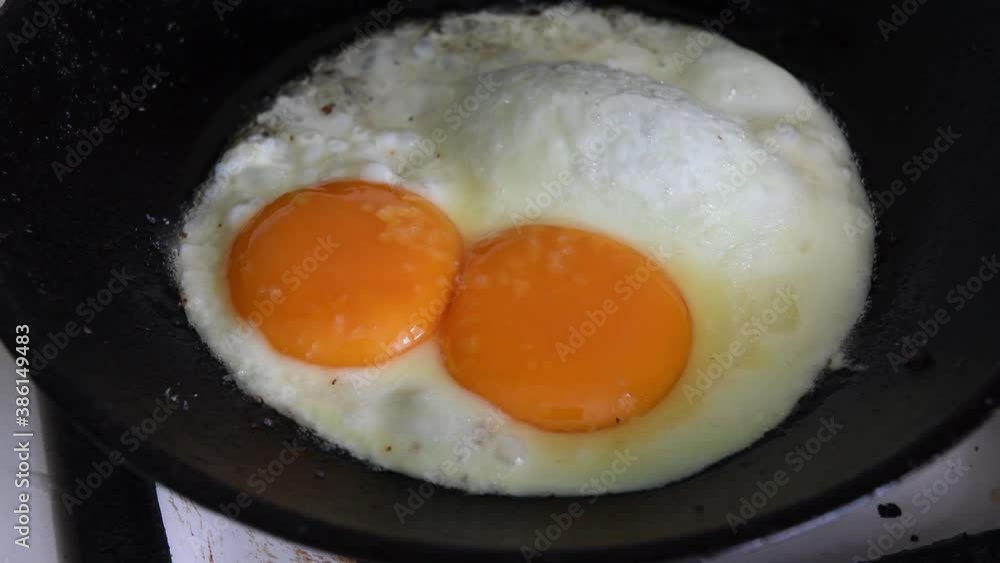 Closeup of fried chicken eggs with big yellow yolks. Frying of chicken eggs in old cast pan with hot oil bubbles. Homemade organic food Closeup of fried chicken eggs with big yellow yolks. Frying of chicken eggs in old cast pan with hot oil bubbles. Homemade organic food