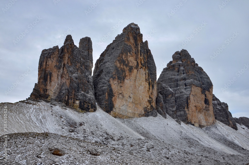 Fototapeta premium Dolomites Alps, Three Peaks (Drei Zinnen), South Tirol, Italy, UNESCO world heritage site, rocky terrain in front, cloudy sky background, autumn landscape