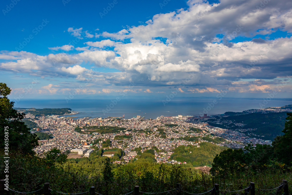 小樽山の展望台から見た、小樽の市街地とその奥にある石狩湾、雲の浮かぶ青空