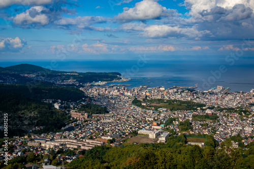 小樽山の展望台から見た、小樽の市街地とその奥にある石狩湾、雲の浮かぶ青空 © 和紀 神谷