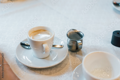 Small white cup of cappuccino stands on the table