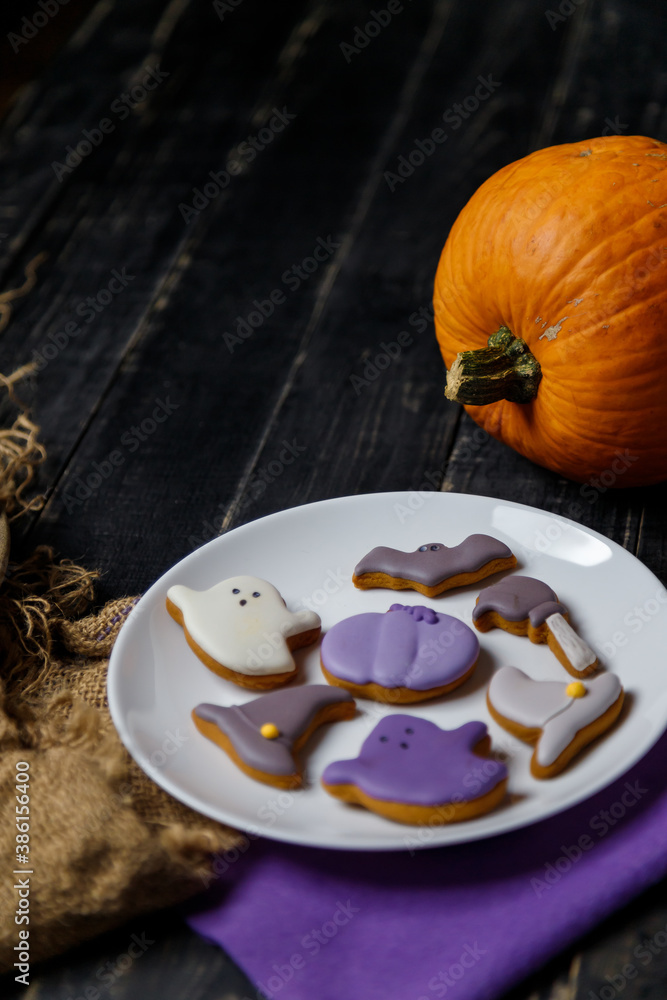Pumpkin and Halloween cookies on white plate, sackcloth on black wooden background. Hallooween trick or treat concept. Copy space. Vertical shot. Pumpkin and Halloween cookies on white plate, sackcloth on black wooden background. Hallooween trick or treat concept. Copy space. Vertical shot.