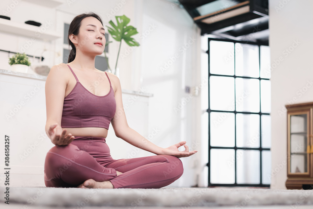 Young attractive smiling woman practicing yoga, sitting in Half Lotus exercise at home. Concept of healthy life and natural balance between body and mental development. Full length Young attractive smiling woman practicing yoga, sitting in Half Lotus exercise at home. Concept of healthy life and natural balance between body and mental development. Full length