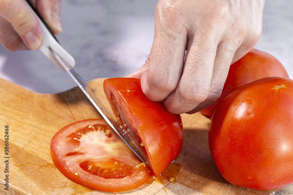 Woman's hands cutting fresh tomato slices Woman's hands cutting fresh tomato slices