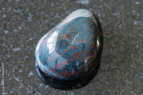 macro photography of sample of natural mineral from geological collection - tumbled Heliotrope (Bloodstone) gemstone on black granite background