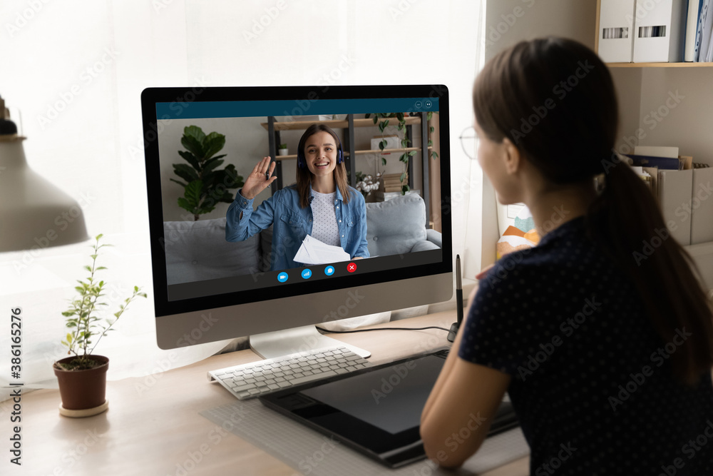 Rear view businesswoman making video call to colleague at home, overjoyed woman waving hand on computer screen, greeting partner, students studying together, working on project online together