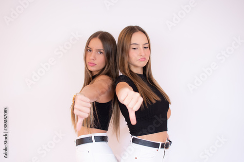Discontent girls shows disapproval sign, keeps thumb down, expresses dislike, frowns face in discontent, dressed in black shirt, isolated over white background. Body language concept.